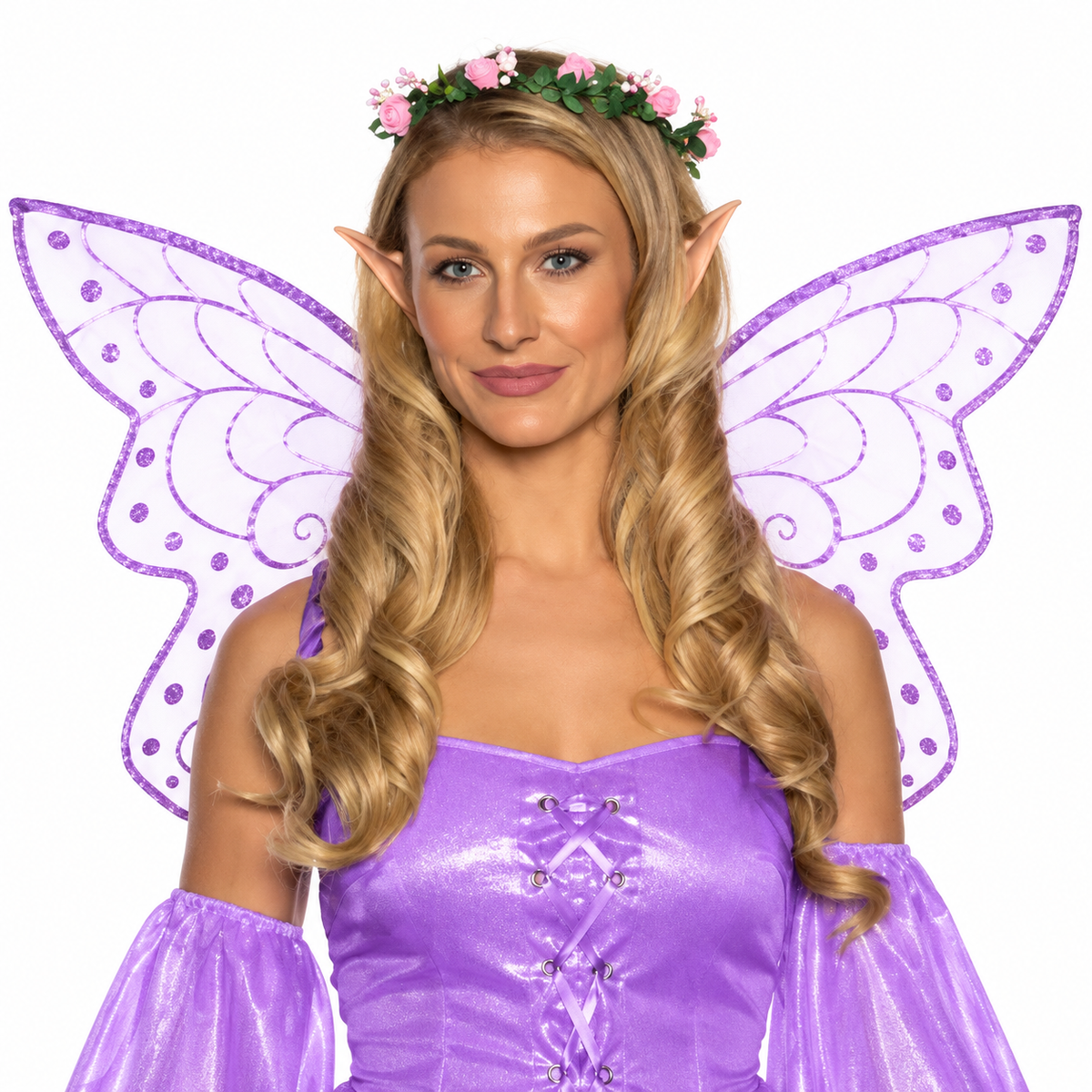 A woman modeling a fairy costume with a shiny purple off-the-shoulder dress, matching purple wings, pointed elf ears, a floral headband, and long blonde wavy hair, photographed against a plain white background.
