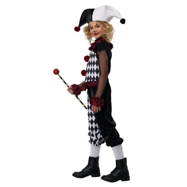 A child modeling a black and white harlequin jester costume, holding a small jester staff, against a plain white background.