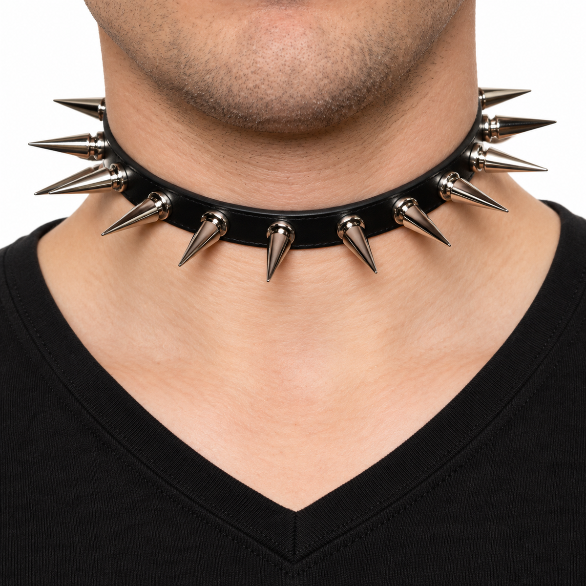 A close-up of a person's neck and chest wearing a black choker collar with multiple pointed silver metal spikes, paired with a black V-neck shirt against a white background.