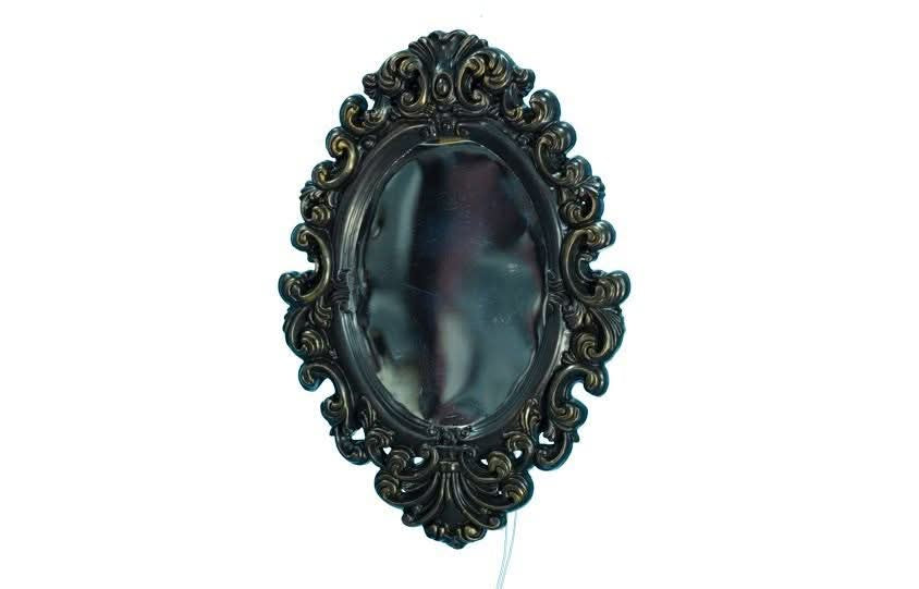 An ornate oval wall mirror with a dark, heavily carved baroque-style frame, shown against a plain white background.