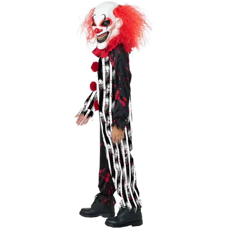 A child modeling a scary clown costume against a plain white background. The costume includes a white and red clown mask with a wide grin, bright red hair, a black and white striped jumpsuit with red blood-like splatters, and black shoes.