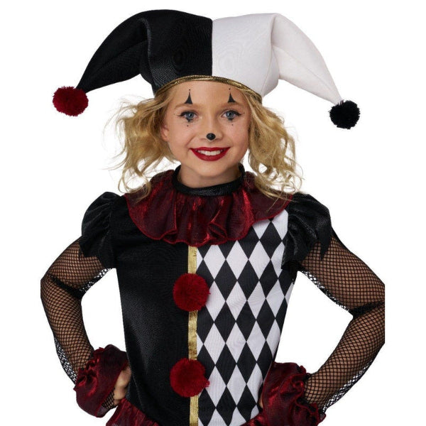A child wearing a jester costume against a plain white background. The costume includes a black and white harlequin-patterned bodice with red pom-pom accents, a black and white jester hat, and a dark red ruffled collar.
