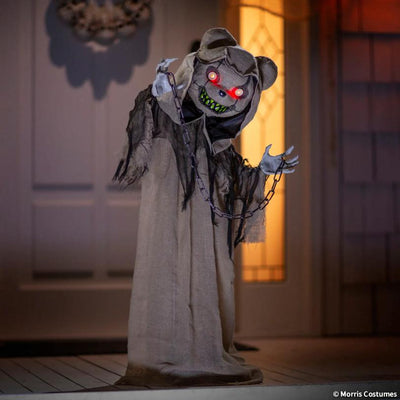 A spooky Halloween decoration shaped like a ragged ghost bear in a tattered robe, with glowing red eyes, green teeth, and a chain around its neck, posed in front of a house door and window.