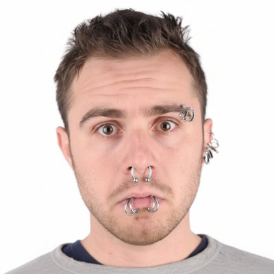 A man wearing multiple body piercings, shown beside the retail packaging of a 'dress me up' body piercing set. The package contains six silver-toned piercing rings on a black backing card.
