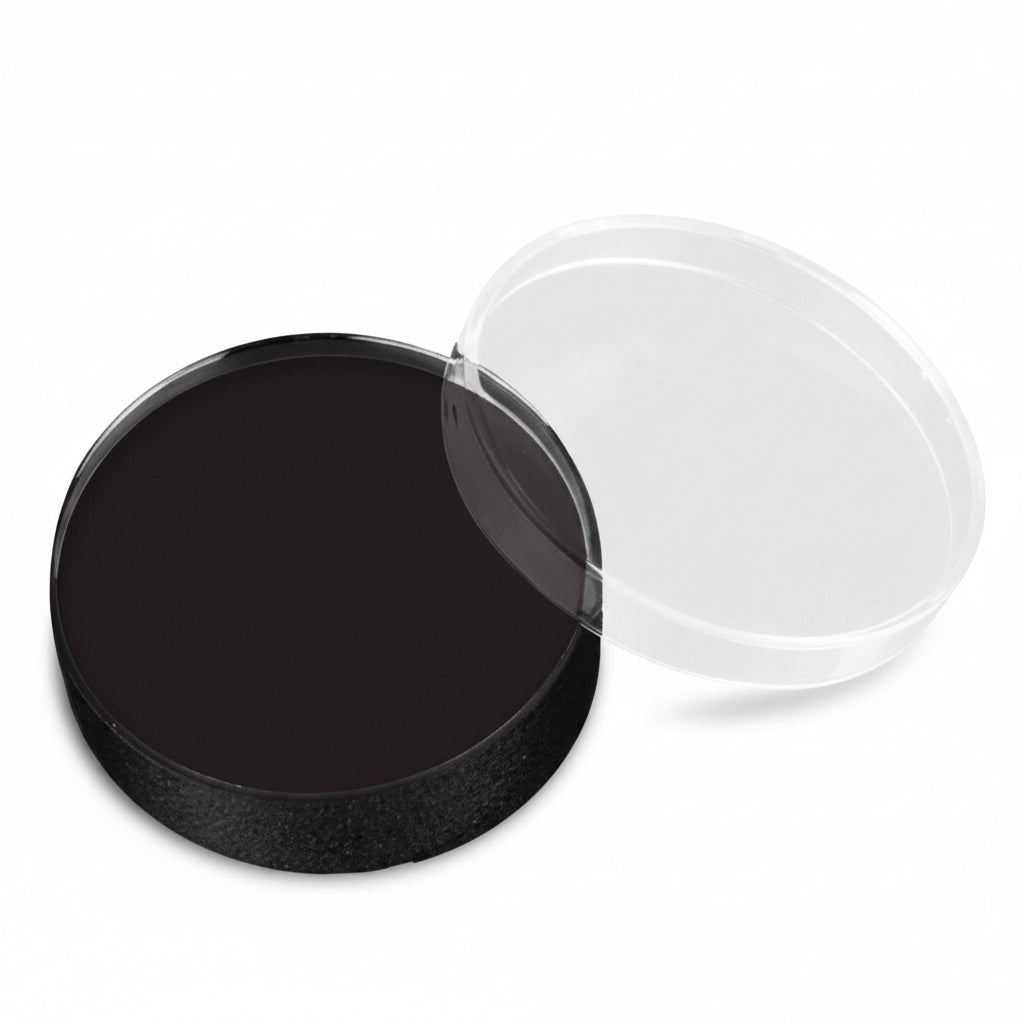 A round black cosmetic pan with a clear plastic lid resting beside it on a white background.