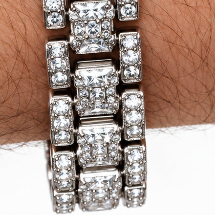 A close-up of a wrist wearing a silver-toned watch heavily embellished with clear crystals, featuring a circular crystal-encrusted face with a dollar-sign motif in the center.